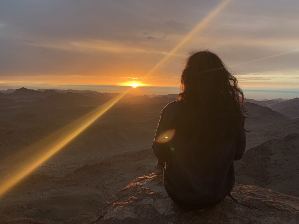 girl sitting on mount sinai as a sun star rises across the desert