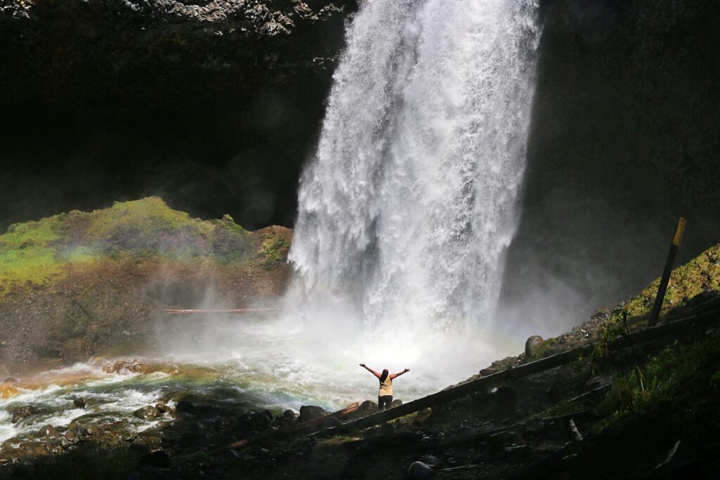 girl with arms outstretched in front of a large waterfall
