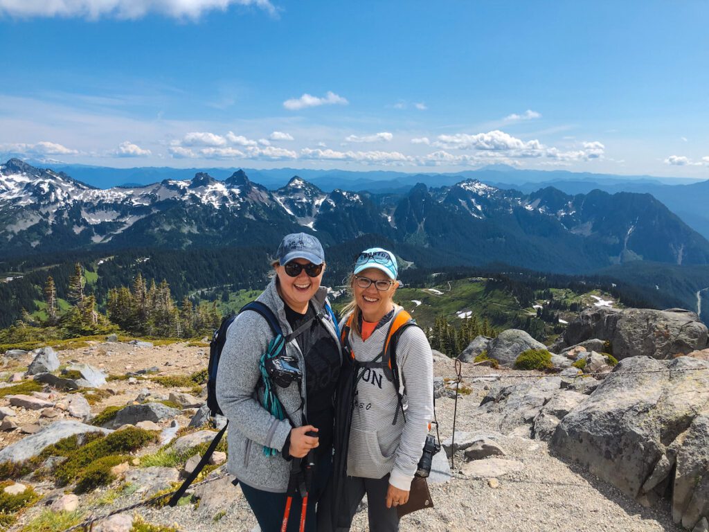 travelers smiling for a picture at the top of mt rainier with mountains in the background